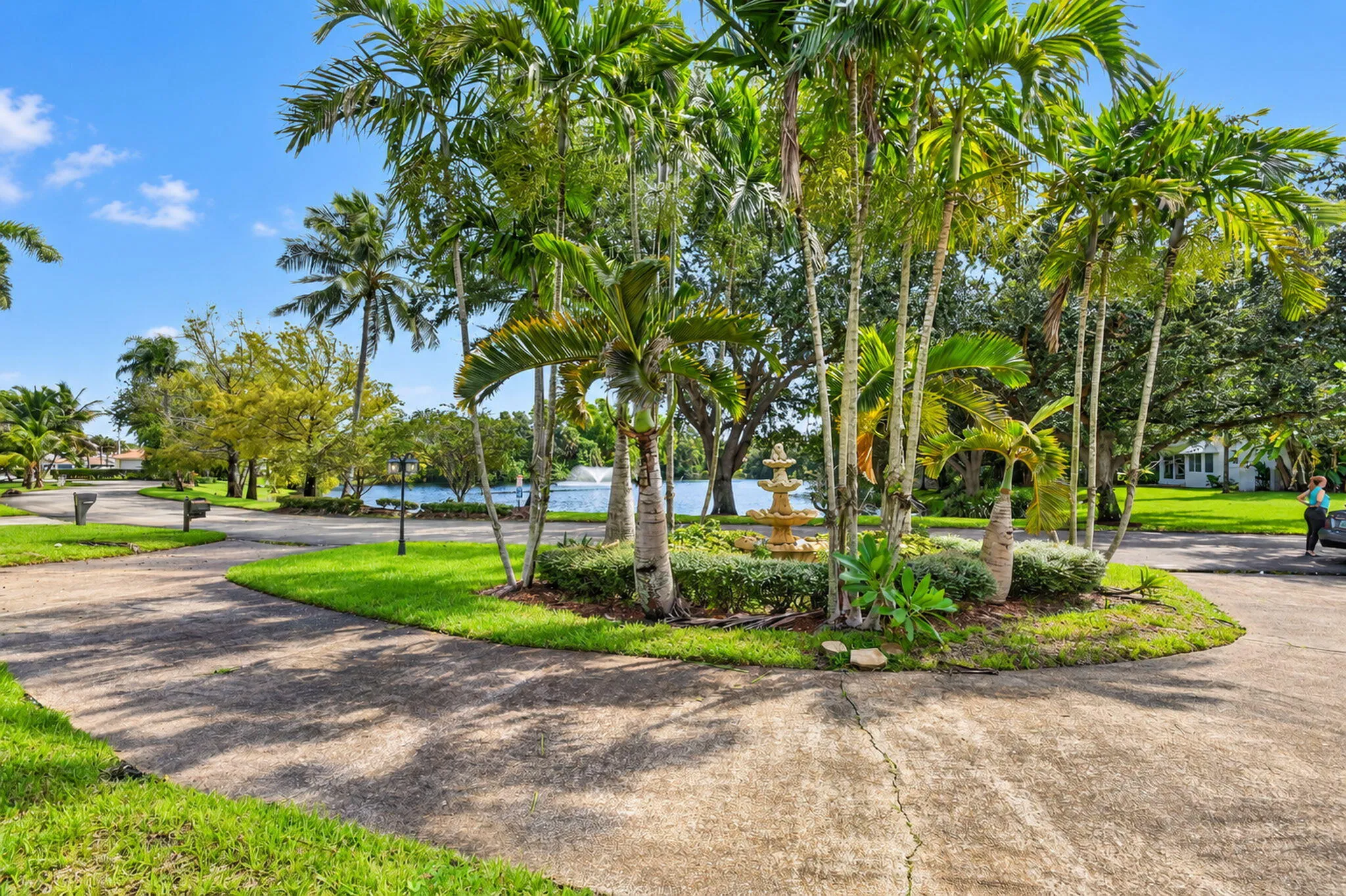 Concrete drive, mature palm trees, manicured landscaping, tiered fountain, water frontage