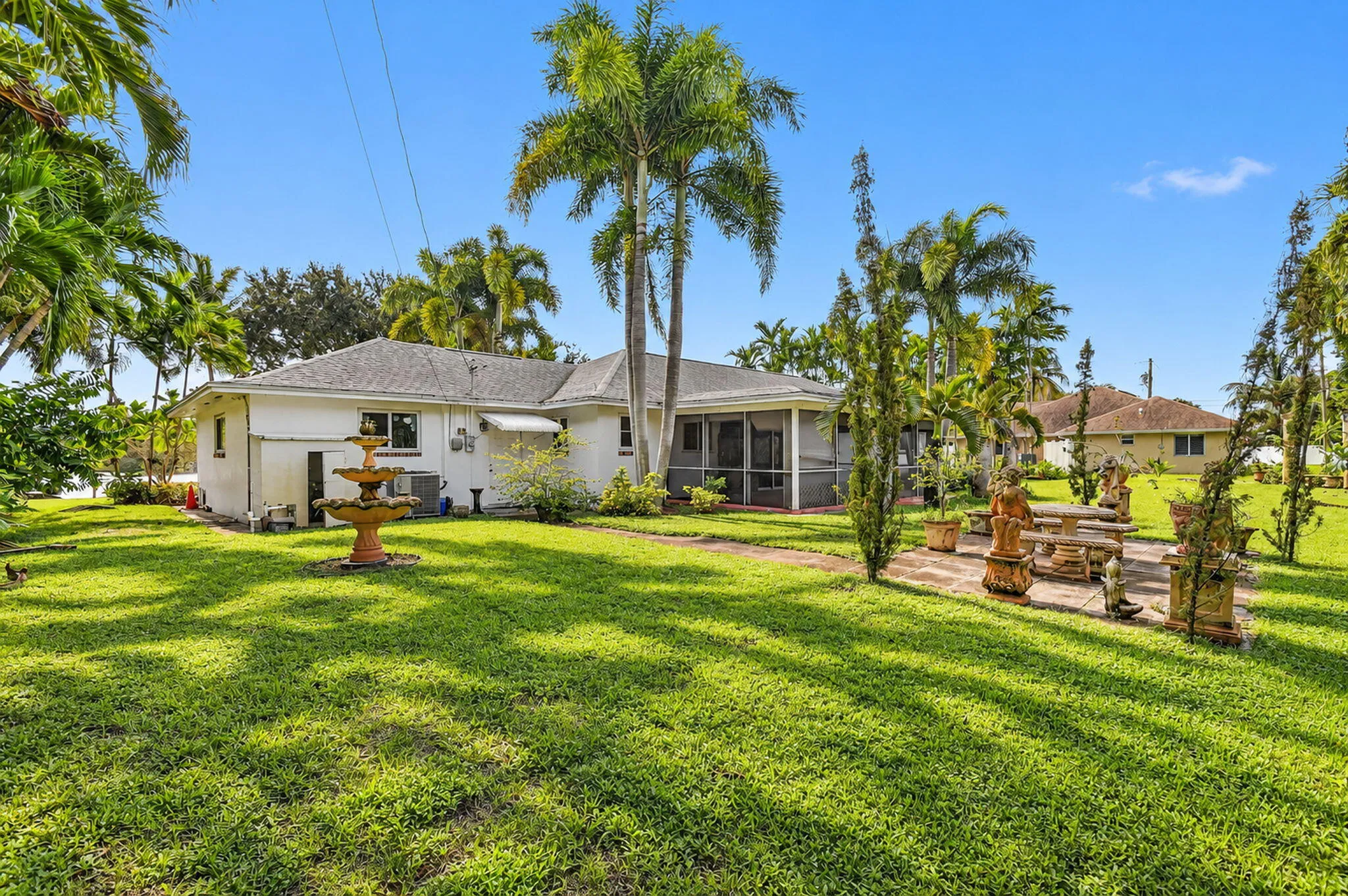 Expansive lawn with mature palm trees, a tiered fountain, and a screened-in patio