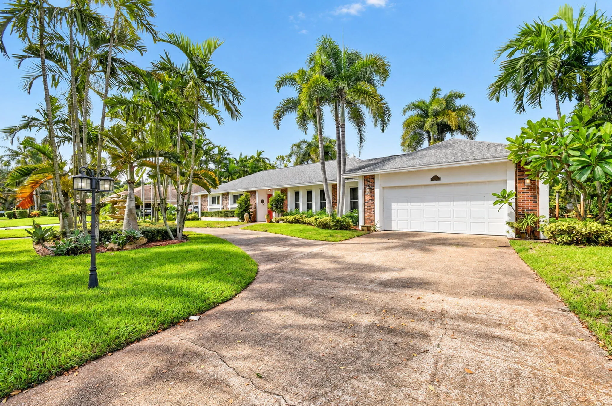 Expansive driveway with a curved path, mature palm trees, exterior brick accents, and an attached two-car garage