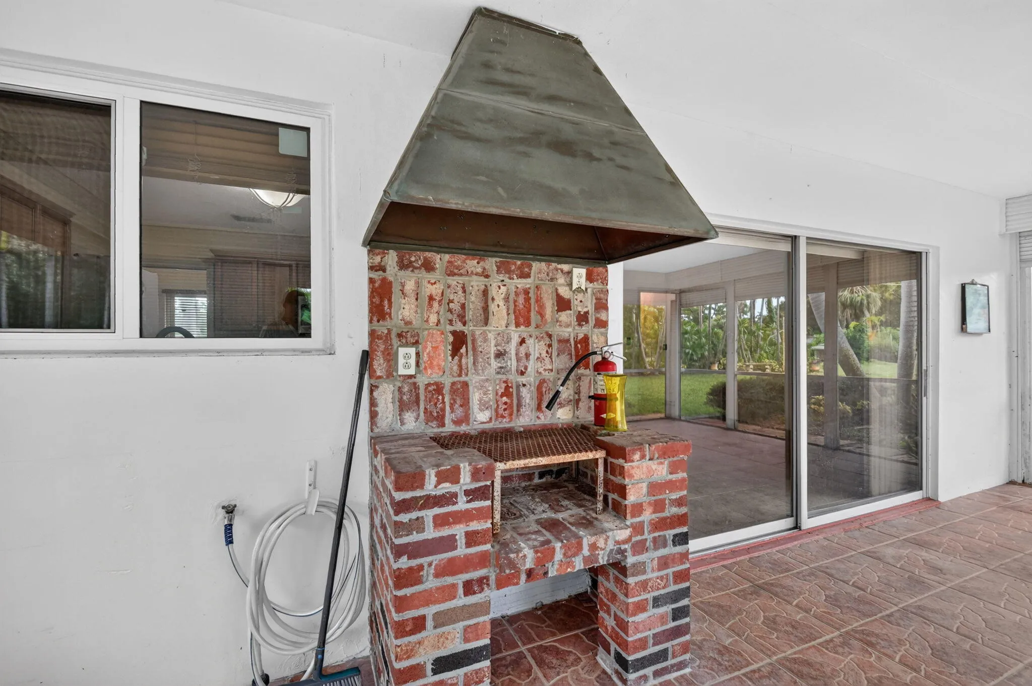 Built-in brick barbecue with metal hood, red tile flooring, and sliding glass doors to a screened enclosure