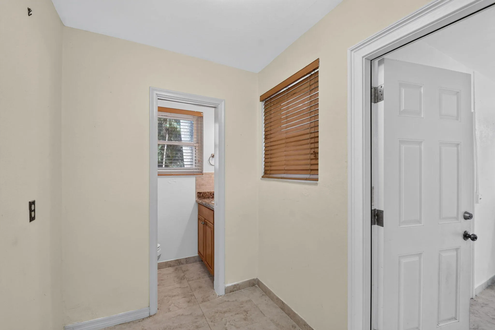 Tile flooring, neutral wall paint, wood window blinds, paneled interior doors, and a recessed doorway with an interior window
