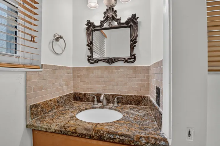 Vanity with an integrated sink, stone countertop, wood-finish cabinetry, and decorative mirror