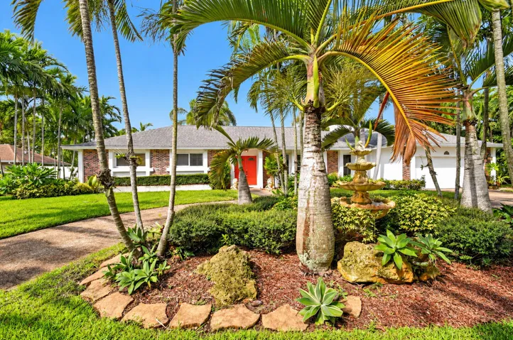 Expansive front yard with a tiered water feature, mature palm trees, diverse plantings, and a textured pathway