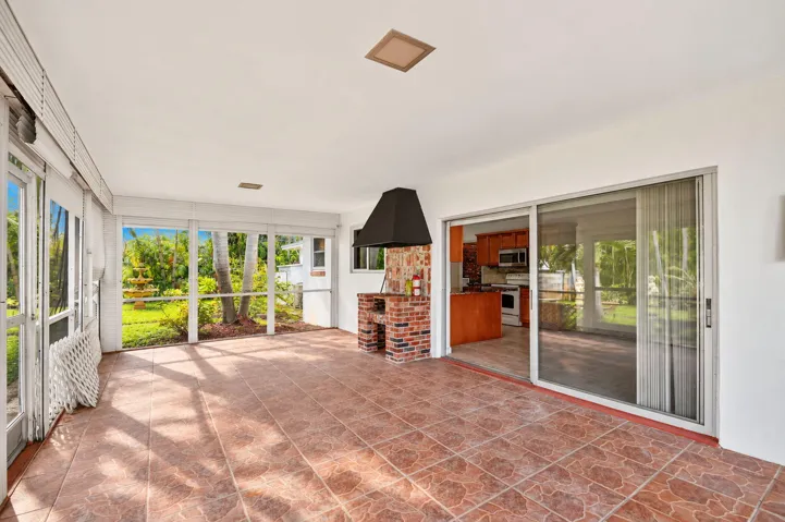 Screened enclosure with ceramic tile flooring, a built-in brick grilling station with an exhaust hood, and a sliding glass door entry to the interior