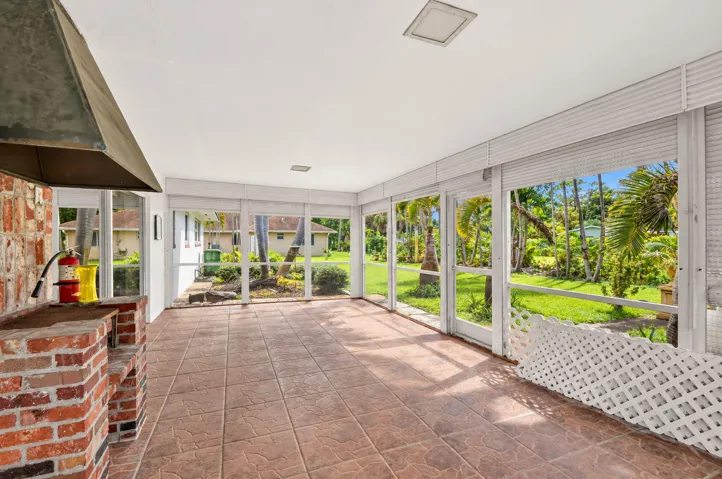 Expansive screened enclosure with a built-in brick grilling station, tile flooring, and a white ceiling