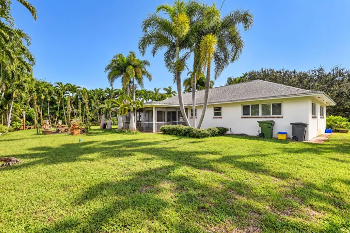 Expansive green lawn with mature palm trees and a screened-in patio