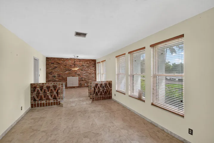 Spacious room featuring neutral-toned flooring, an exposed brick accent wall, and multiple windows with wood trim