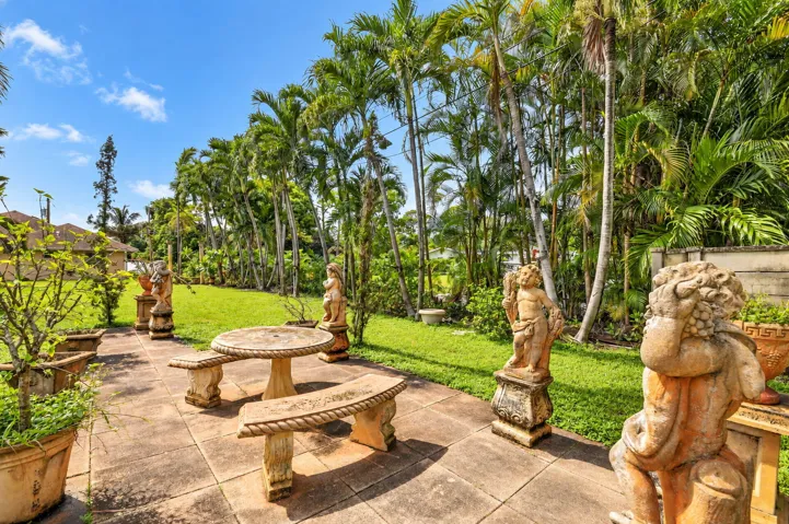 Patio with stone pavers, mature palm trees, grassy area, and decorative statues