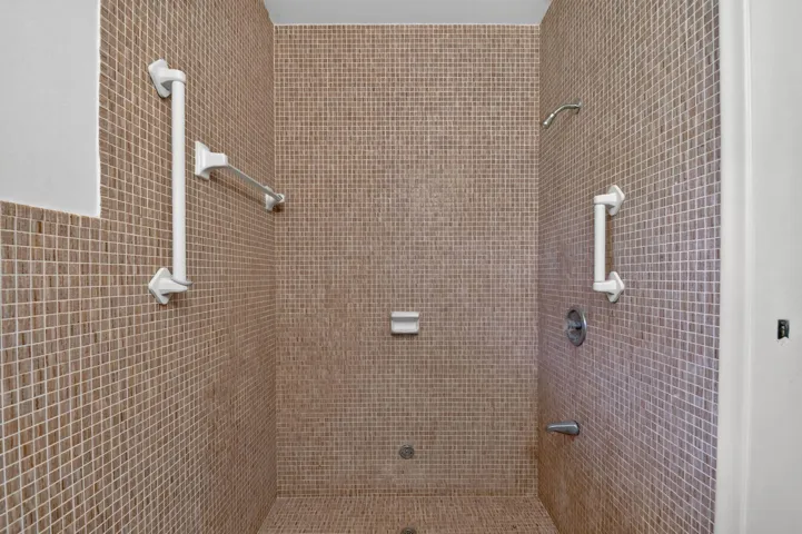 Walk-in shower with full wall and floor mosaic tile, complete with a mounted showerhead and integrated grab bars