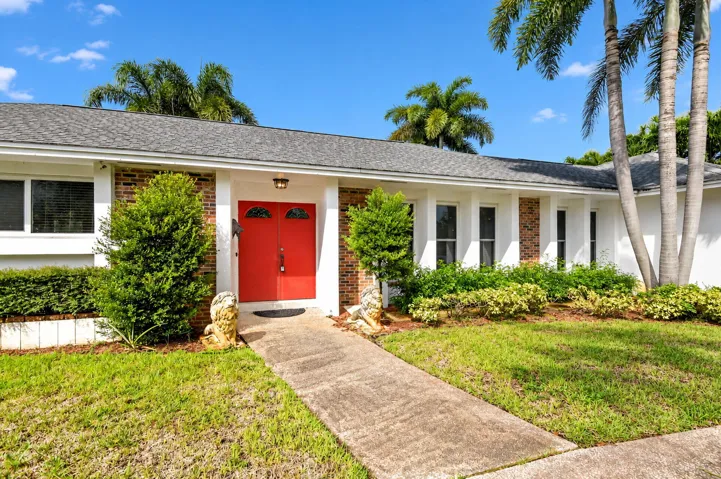 Paved entry walkway leading to a double red front door with arched glass details, flanked by brick facade accents and mature landscaping
