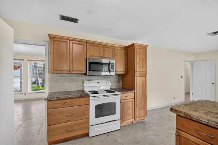 Wood-finish cabinetry with stainless steel microwave, white electric range, and granite-style countertops