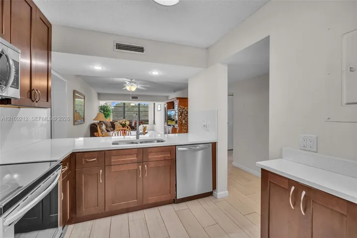 Kitchen featuring wood-finish cabinetry, solid surface countertops, stainless steel appliances, and ceramic tile flooring