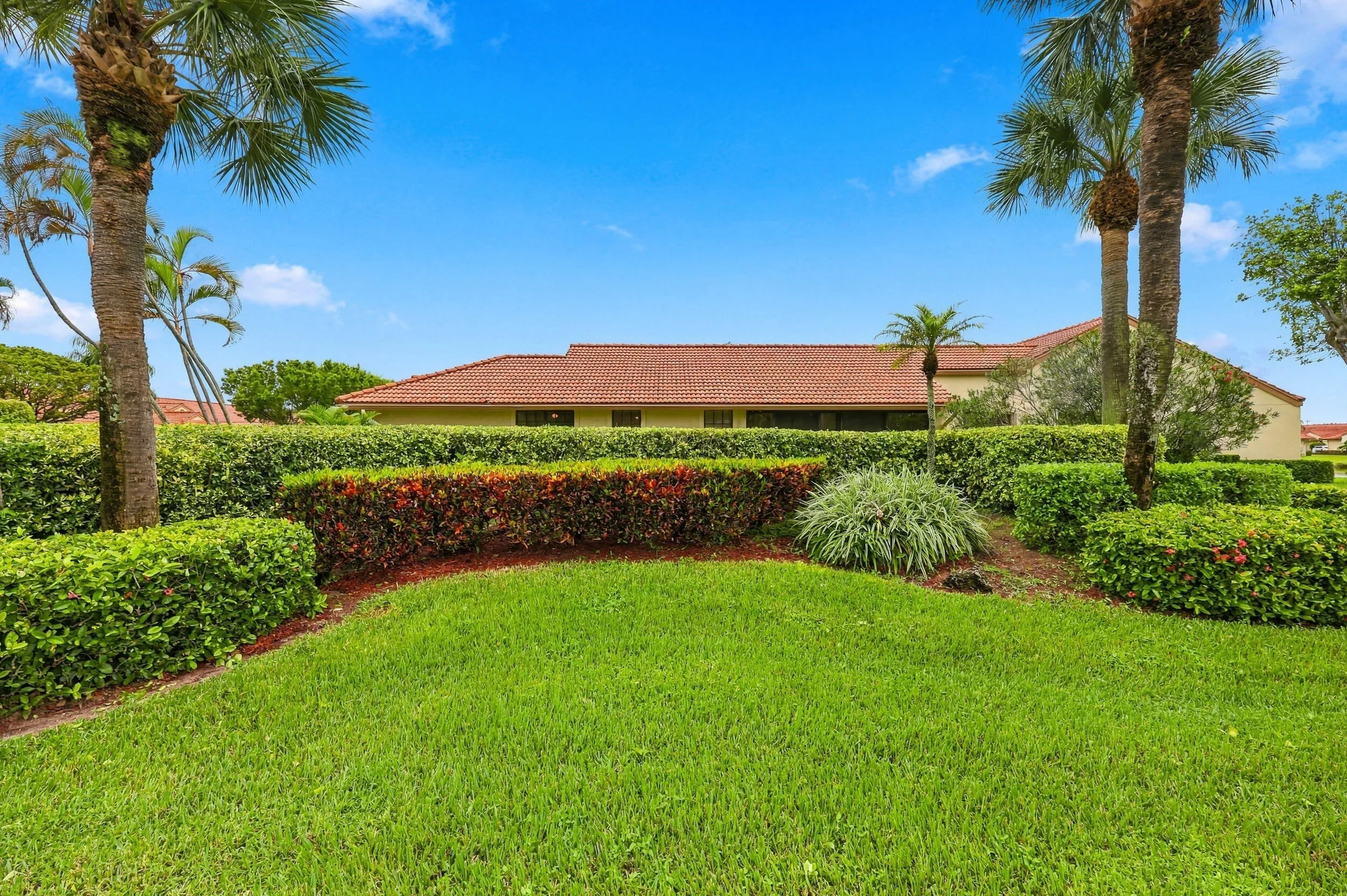 Expansive green lawn with layered hedges, mature palm trees, and a terracotta tile roof