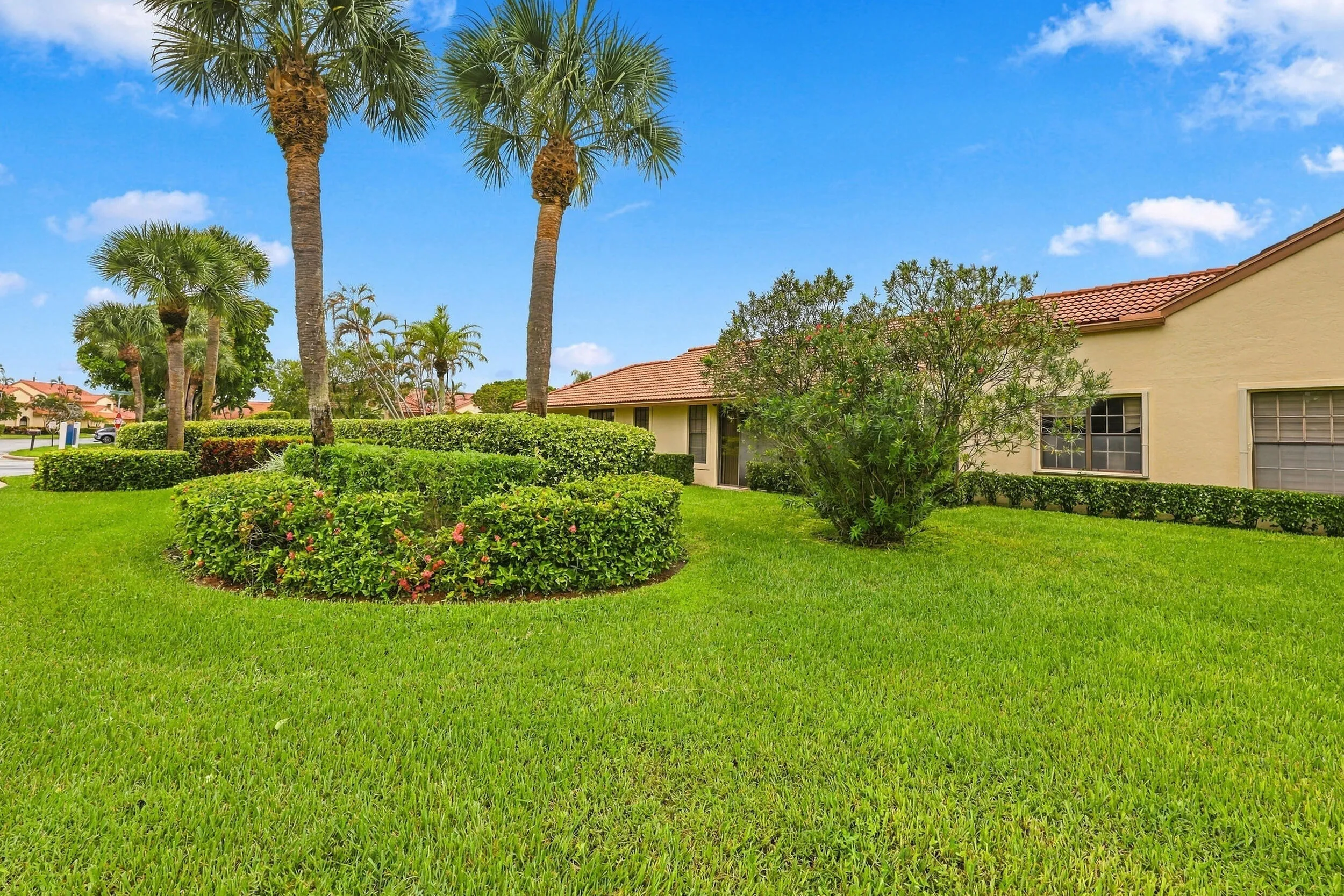 Manicured lawn with mature palm trees, sculpted hedges, and a stucco exterior with a terra cotta tile roof