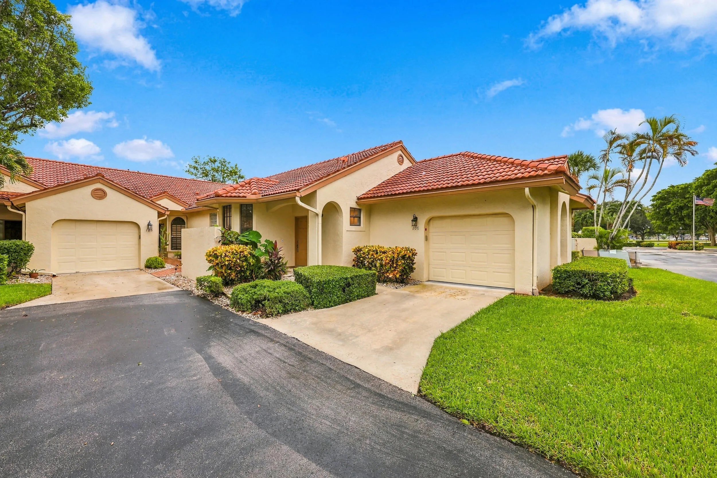 Stucco exterior with a terra cotta tile roof, two attached garages, and a paved driveway