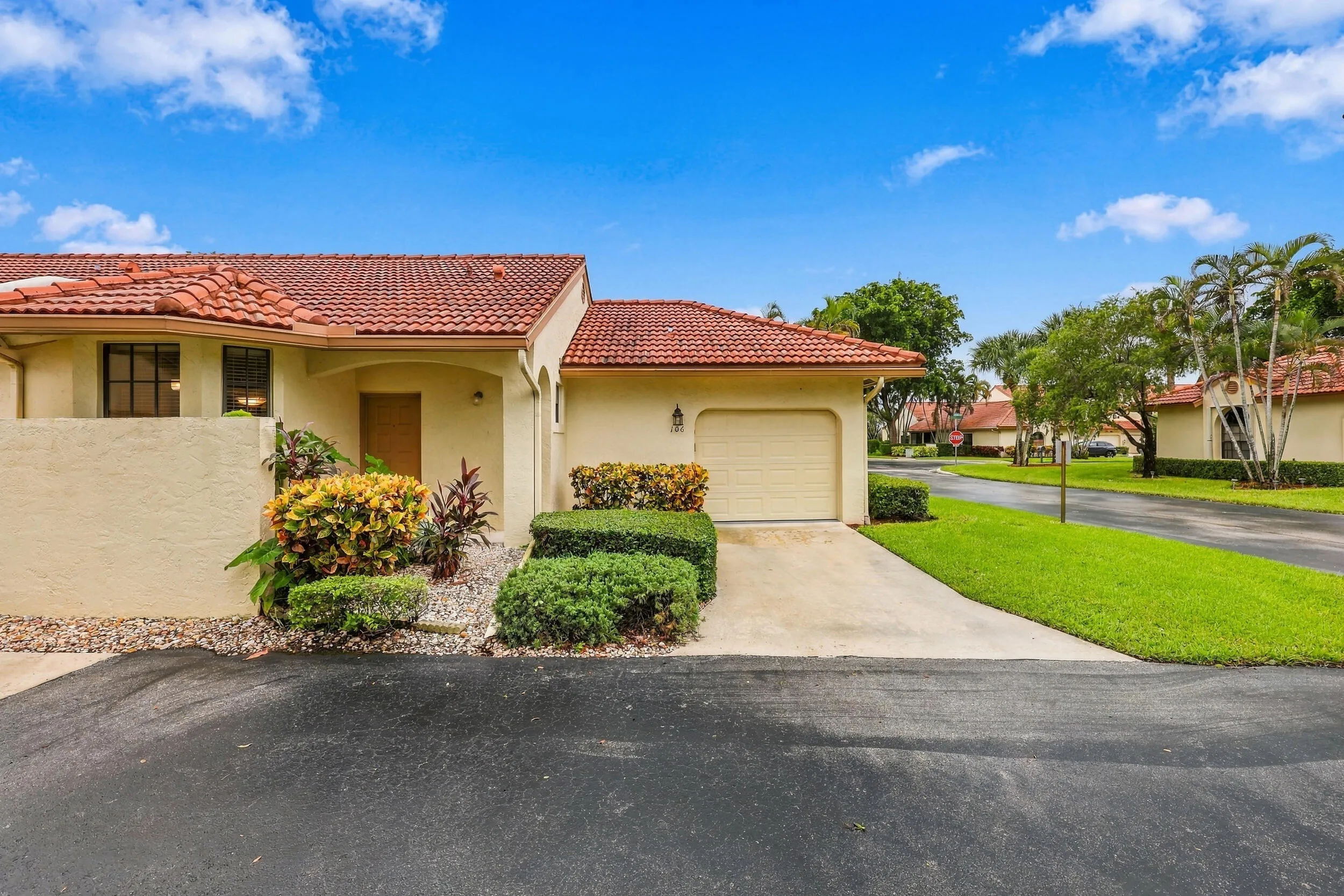Mediterranean-style exterior with a terracotta tile roof, stucco finish, attached garage, concrete driveway, and established landscaping