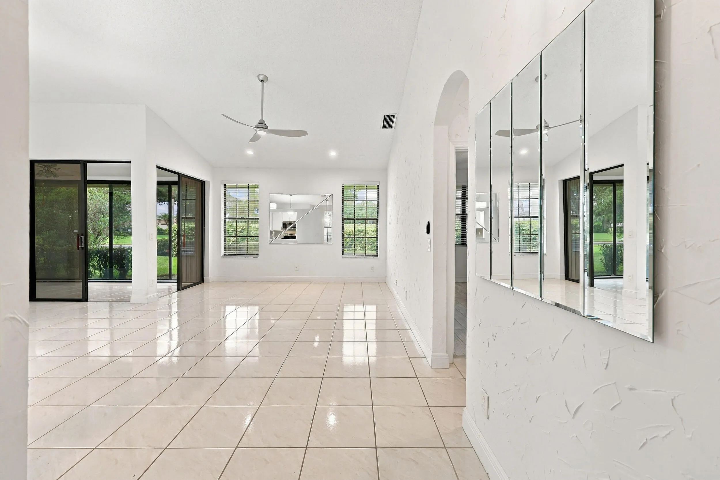 Expansive tiled flooring throughout, modern ceiling fan, large windows with exterior views, built-in wall mirror, and sliding glass doors