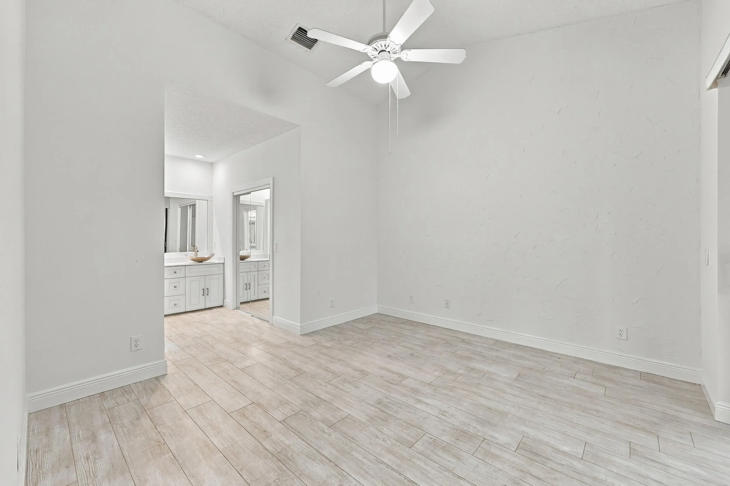 Vaulted ceiling with a ceiling fan, light wood-finish flooring, and white walls