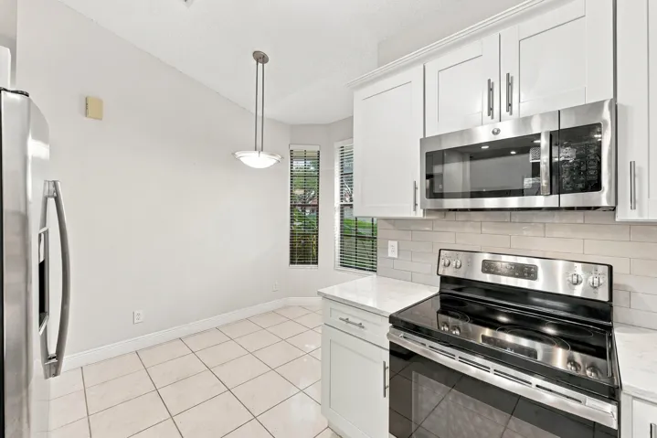 Kitchen featuring white shaker-style cabinetry, stainless steel appliances, a tile backsplash, and light-toned tile flooring
