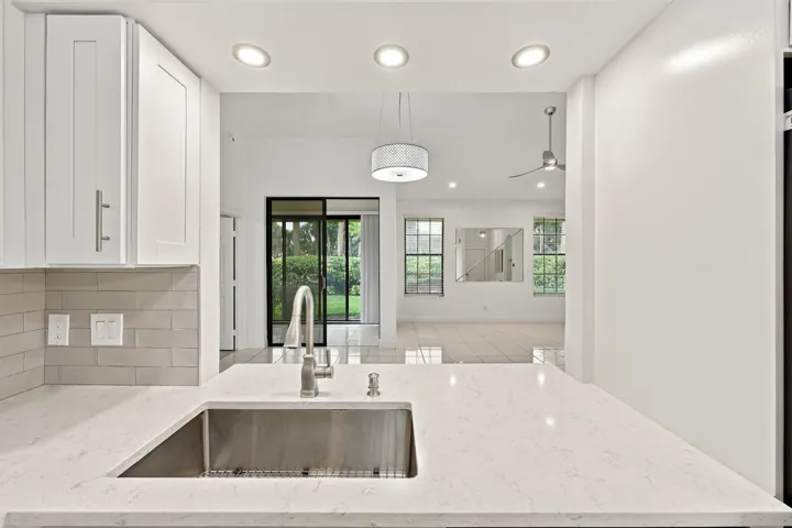 White shaker cabinetry, light-toned subway tile backsplash, stainless steel sink, contemporary faucet, and light-toned countertops