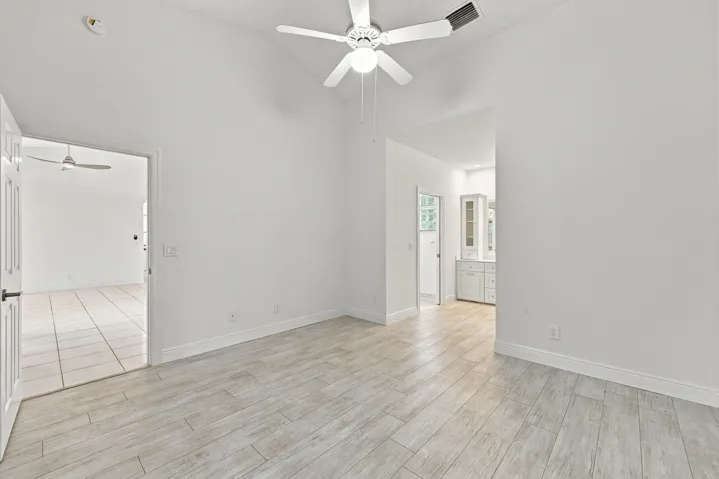 Vaulted ceiling with a ceiling fan, wood-finish tile flooring, white interior walls, and built-in cabinetry with glass-front uppers