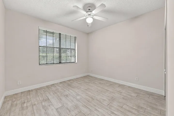 Wood-finish flooring with white baseboards, a window with blinds, and a ceiling fan with integrated lighting