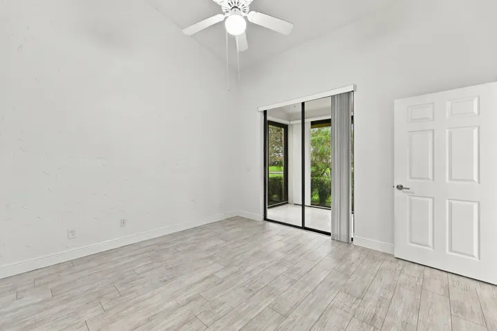 Vaulted ceiling with a white ceiling fan, sliding glass doors to an outdoor area, six-panel interior door, and light wood-finish flooring