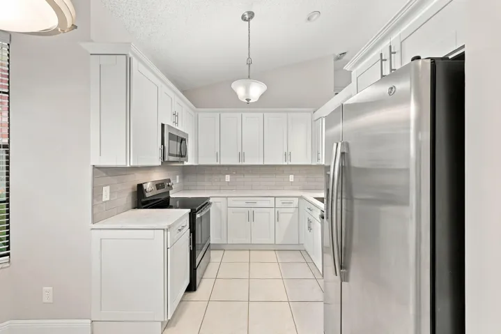 Kitchen featuring white shaker cabinetry, stainless steel appliances, light-toned countertops, tile flooring, and a tiled backsplash