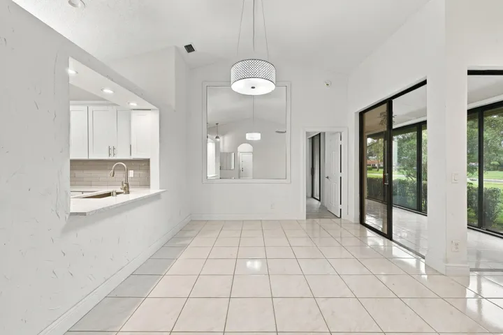 Vaulted ceilings, tile flooring, modern drum pendant light, white shaker cabinetry, and a kitchen pass-through