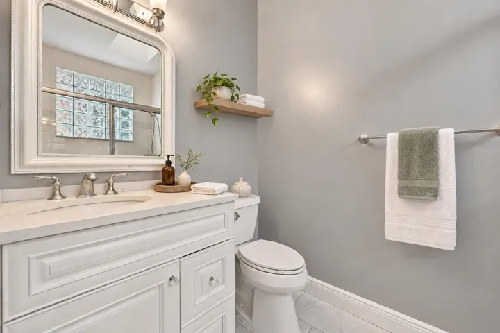 White vanity with paneled doors and crystal knobs, light-toned countertop, and undermount sink with brushed nickel faucet