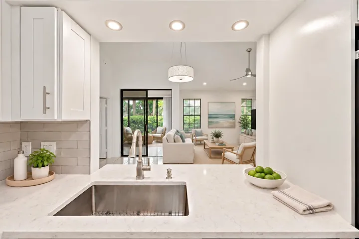 Stainless steel sink with a gooseneck faucet, light-toned countertop, white cabinetry with brushed nickel hardware, and a light subway tile backsplash