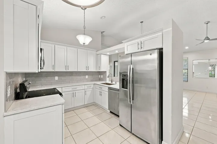 Kitchen with white shaker-style cabinetry, stainless steel appliances, light-toned countertops, tile flooring, and a subway tile backsplash