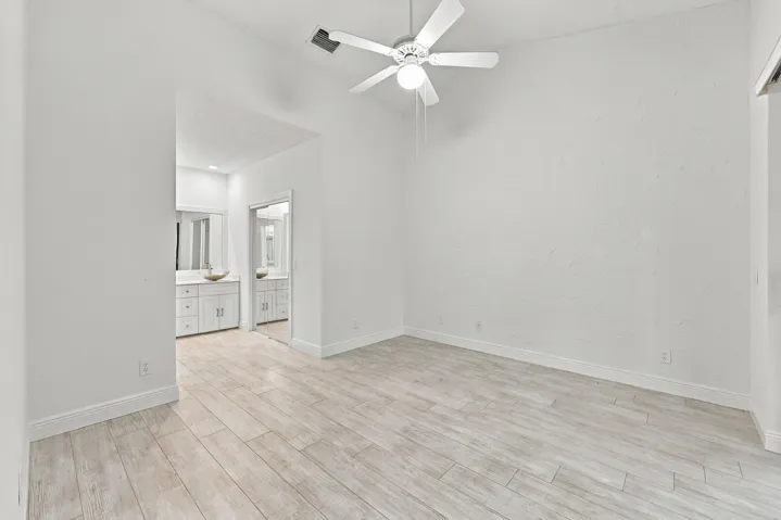 Vaulted ceiling with a ceiling fan, light wood-finish flooring, and white walls