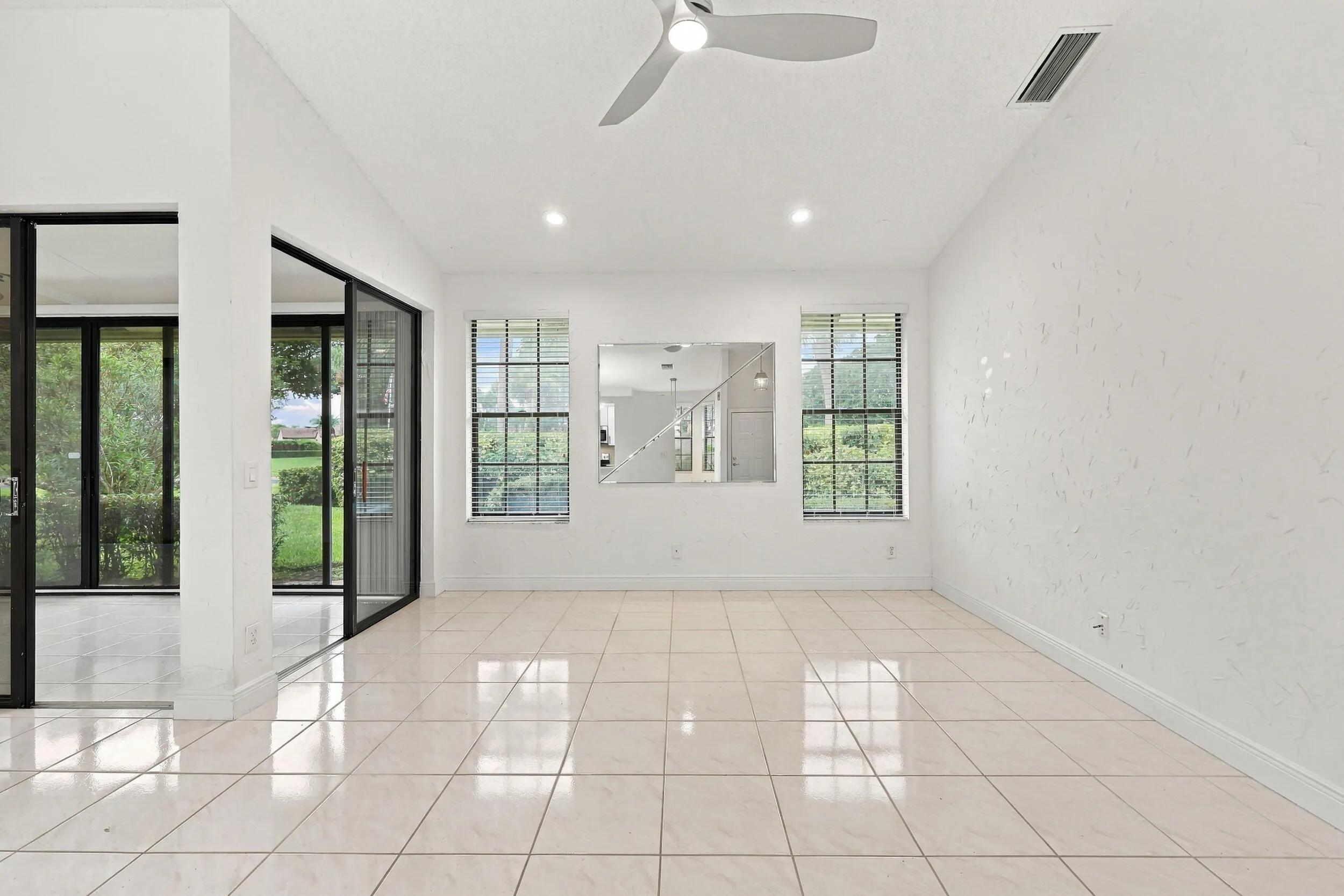 Expansive room featuring light-colored tile flooring, multiple windows with blinds, a ceiling fan, and recessed lighting
