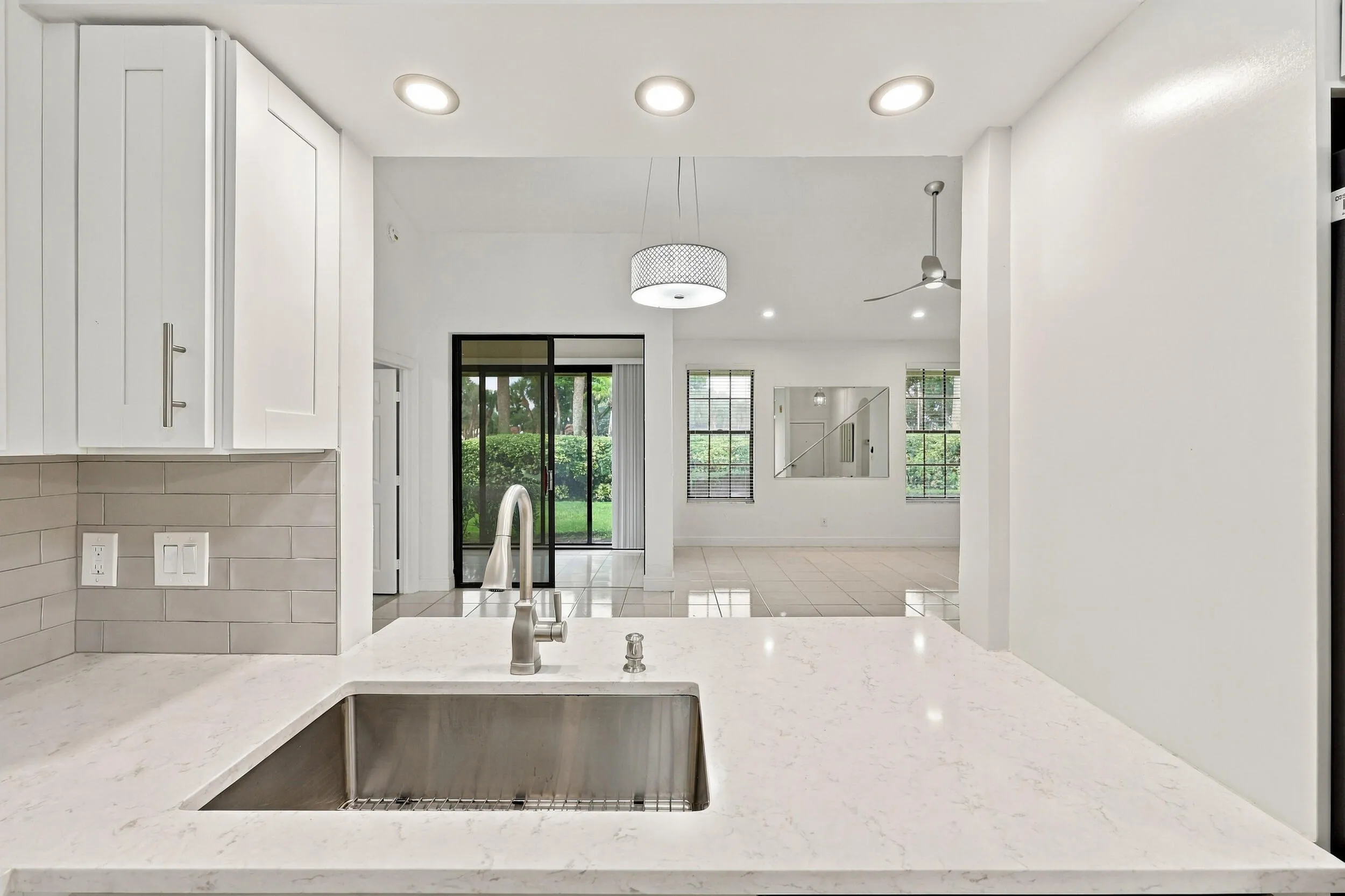 White shaker cabinetry, light-toned subway tile backsplash, stainless steel sink, contemporary faucet, and light-toned countertops