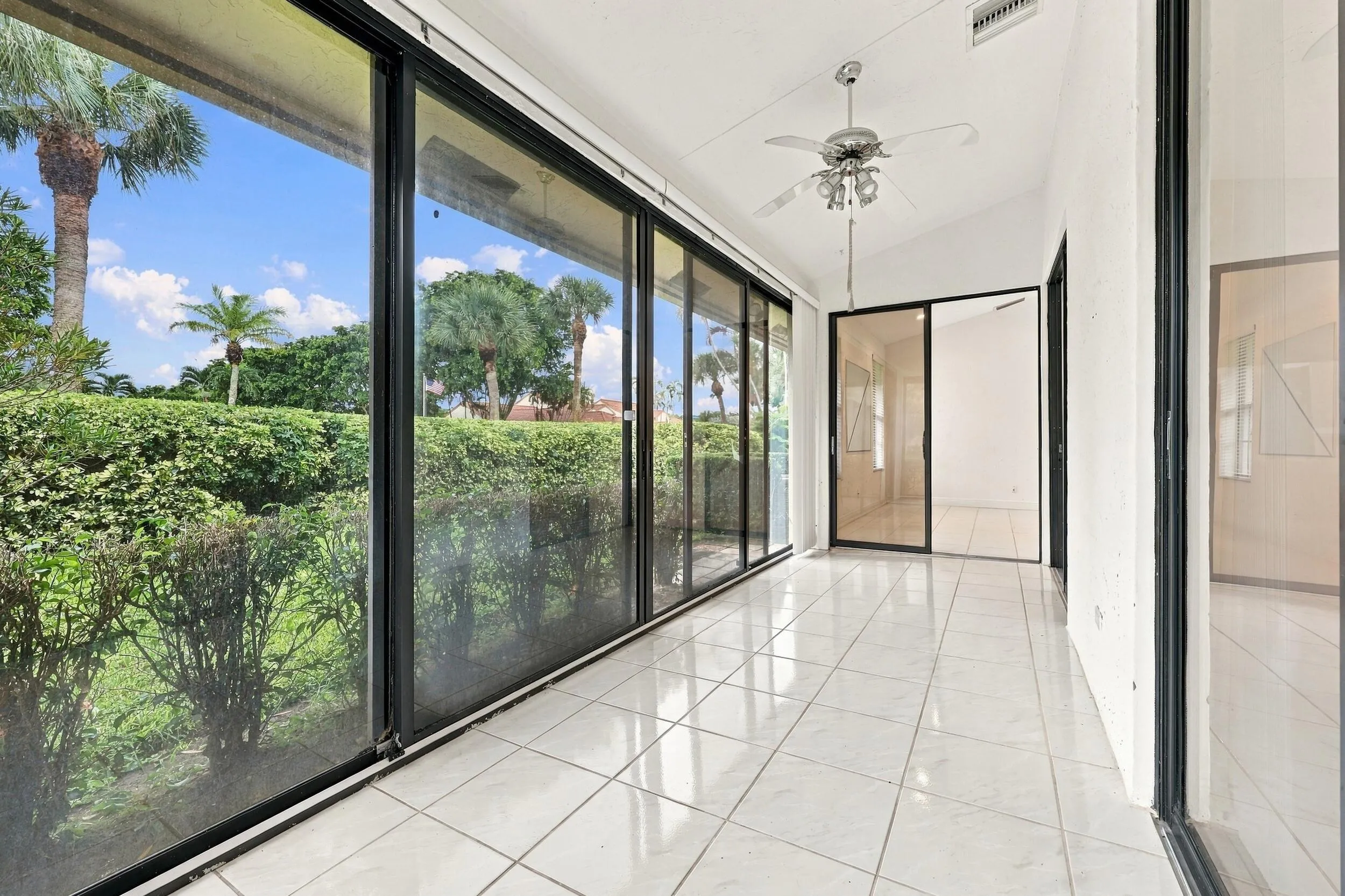 Expansive room with wall-to-wall sliding glass doors, white tiled flooring, a vaulted ceiling, and a ceiling fan with integrated lighting