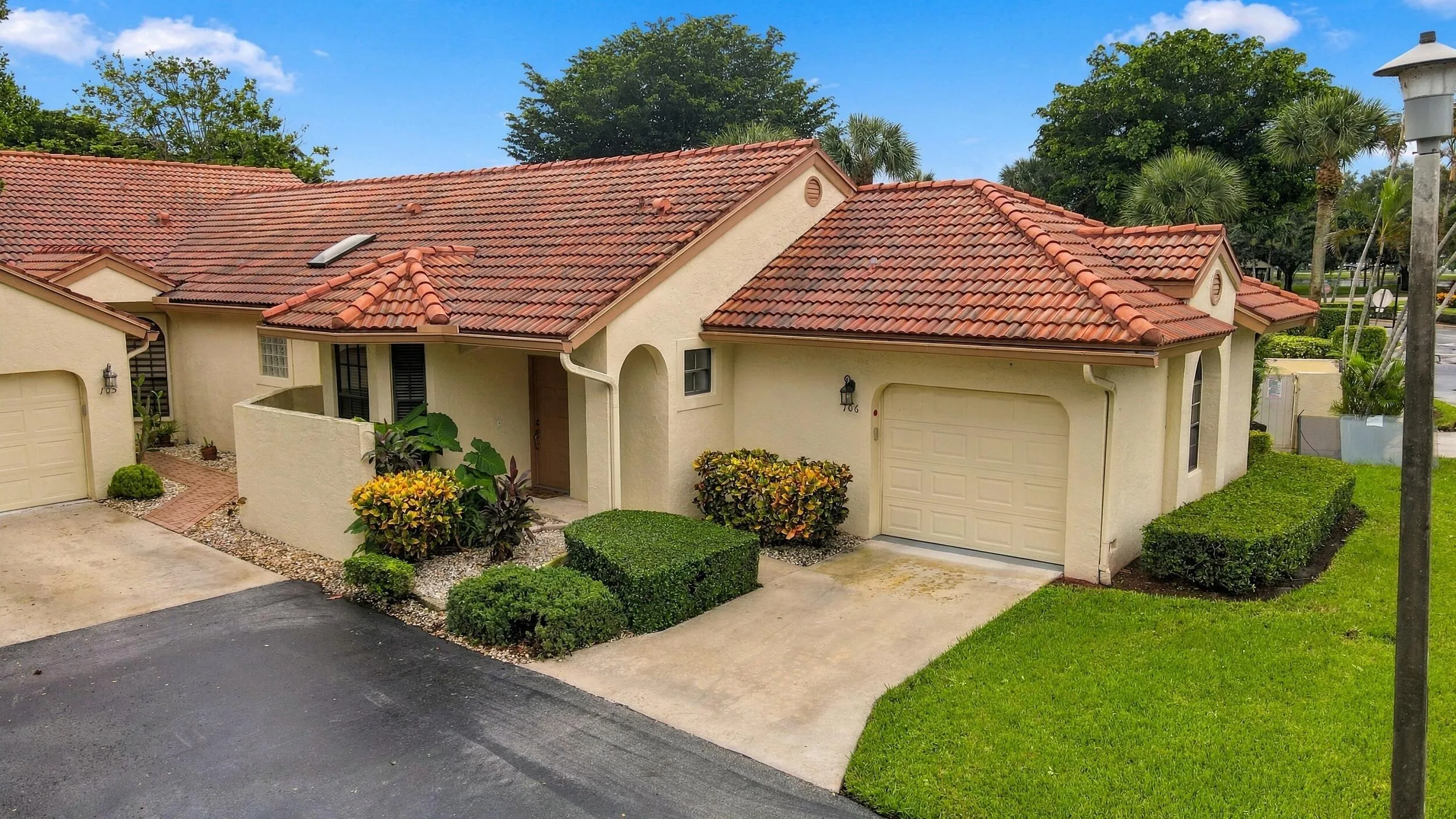 Mediterranean-inspired exterior with a terracotta tile roof, stucco facade, attached garage, and manicured landscaping