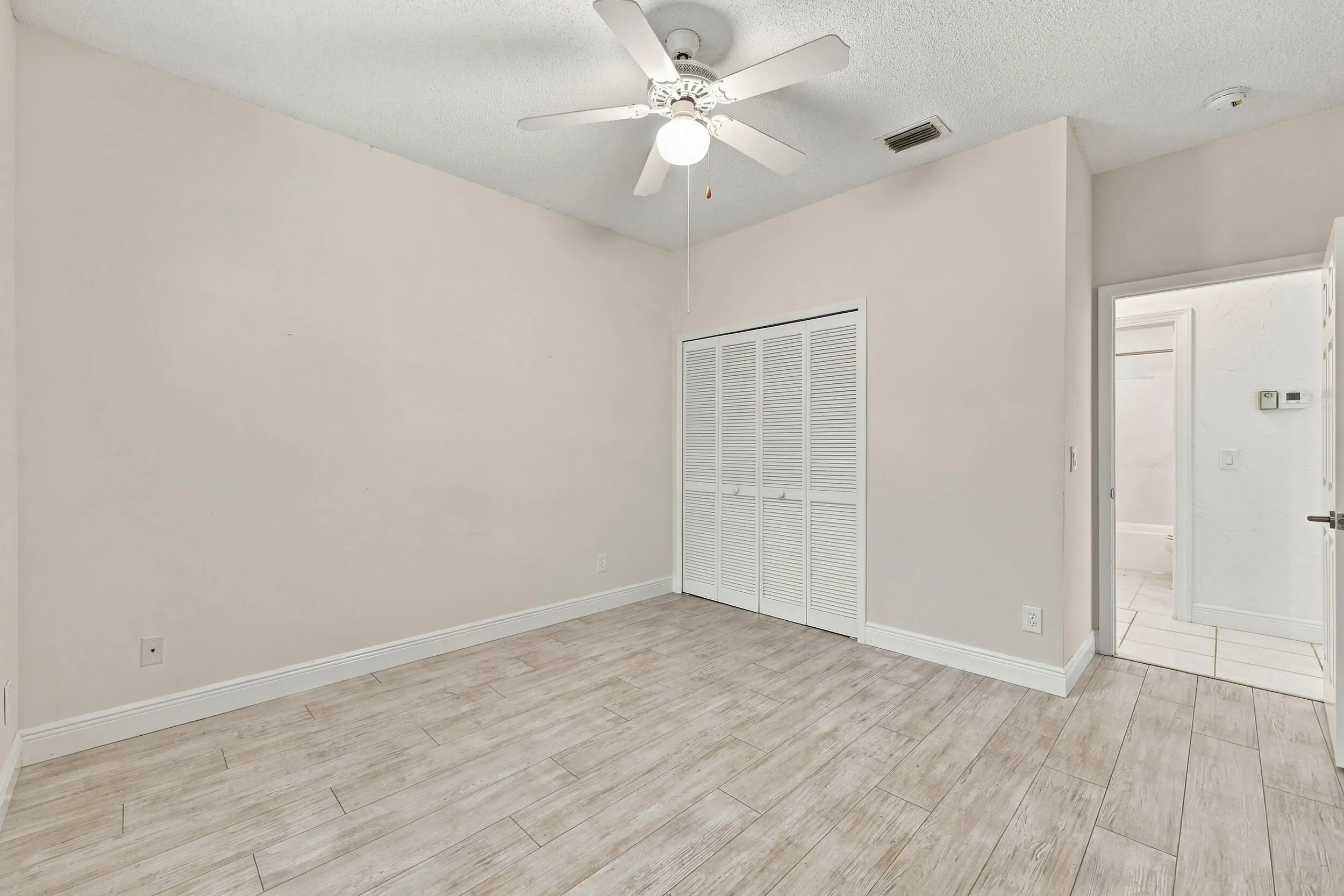 Wood-finish flooring, ceiling fan with integrated lighting, louvered bi-fold closet doors, and recessed ceiling vent