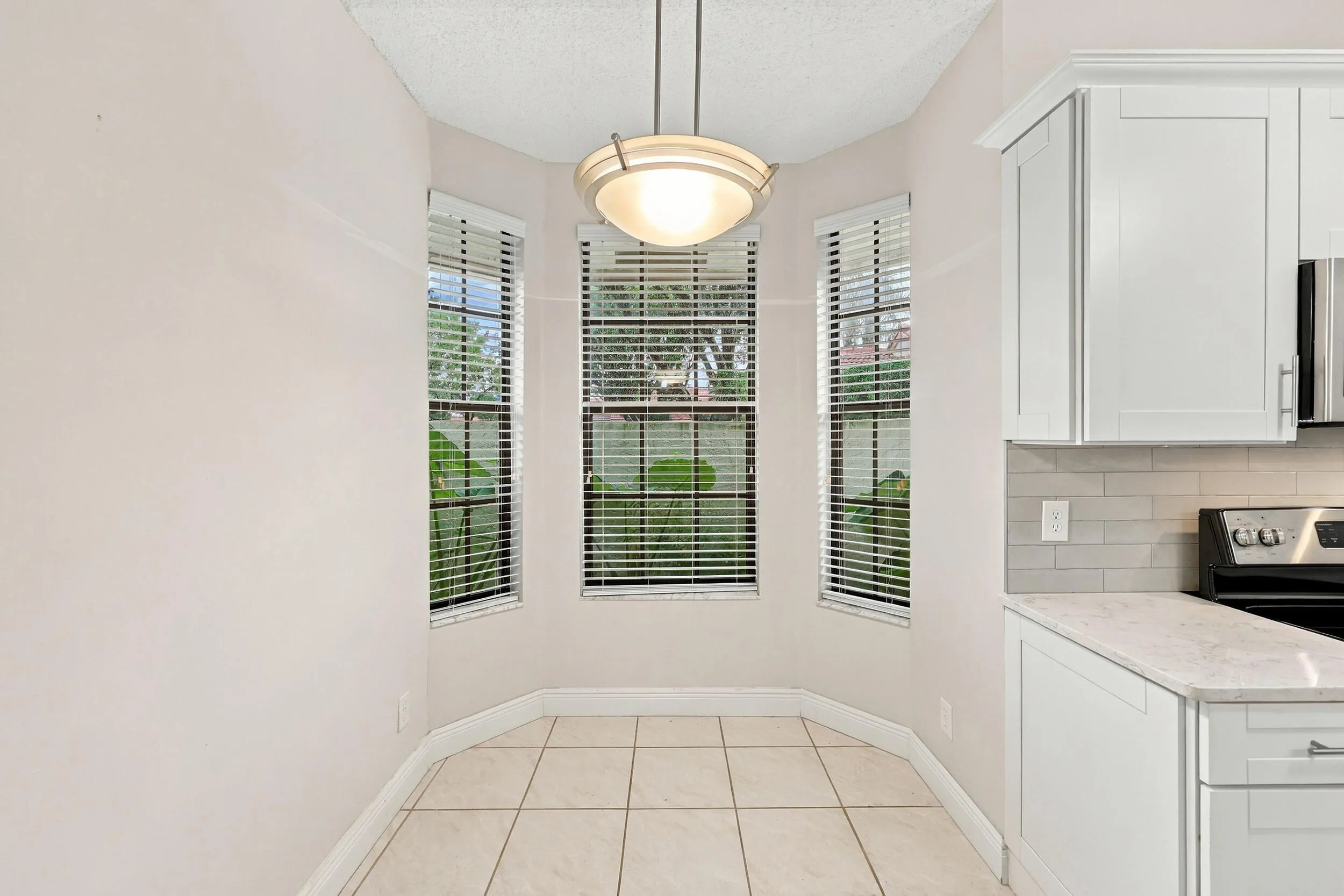 Bay window area with tile flooring, featuring a contemporary pendant light fixture, white cabinetry, and a light-toned countertop