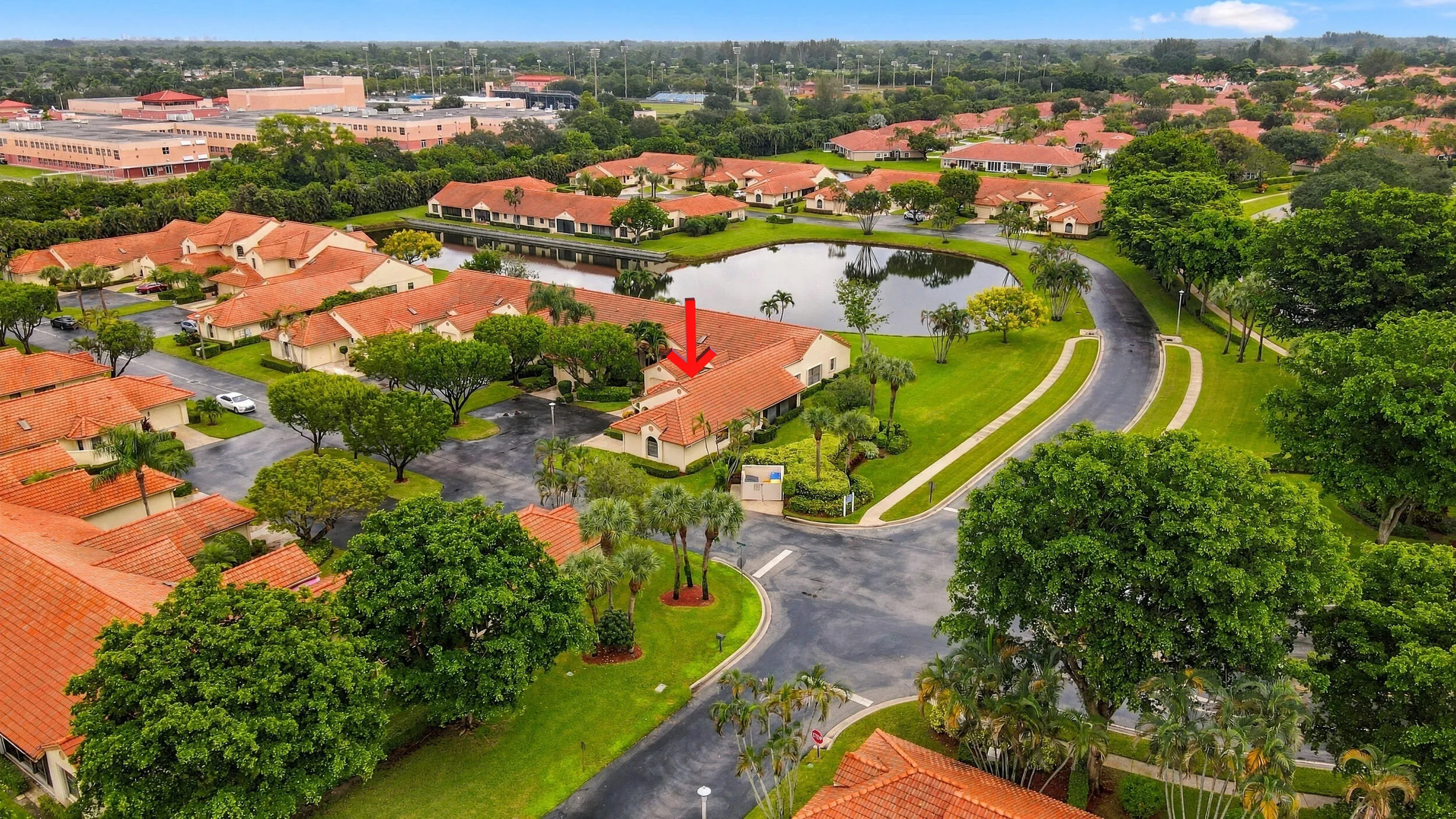Residential community featuring a central pond, paved roads, and lush landscaping