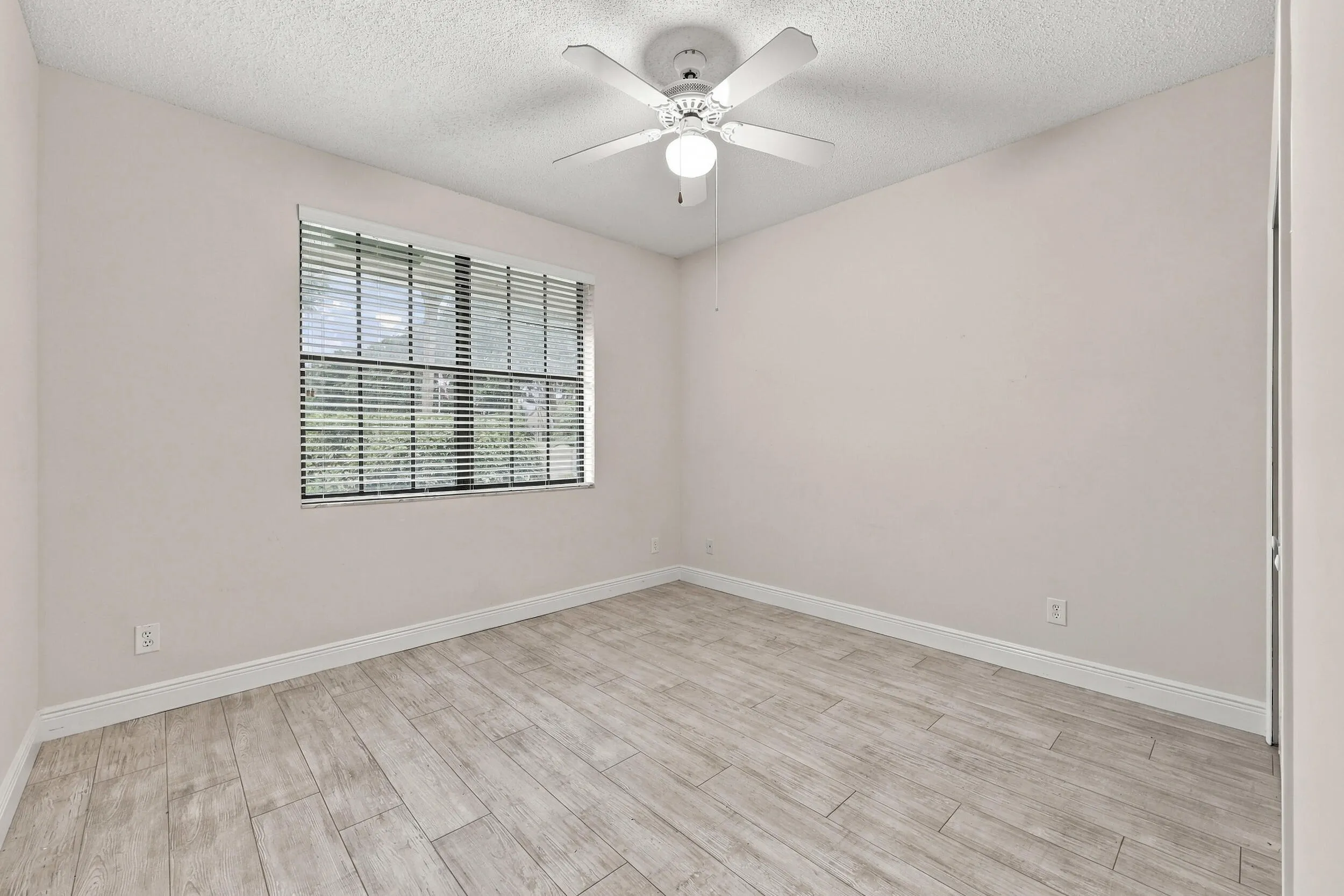 Wood-finish flooring with white baseboards, a window with blinds, and a ceiling fan with integrated lighting