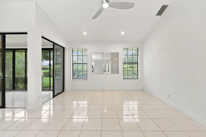 Expansive room featuring light-colored tile flooring, multiple windows with blinds, a ceiling fan, and recessed lighting