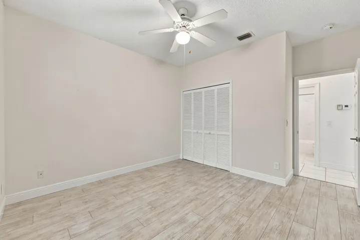 Wood-finish flooring, ceiling fan with integrated lighting, louvered bi-fold closet doors, and recessed ceiling vent