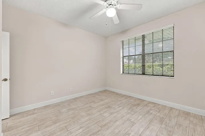 Neutral wall tones, wood-finish flooring, ceiling fan with integrated lighting, window with horizontal blinds, and white trim throughout