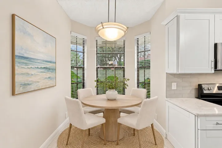 Bay window with three vertical windows, white cabinetry with silver hardware, light-colored countertops, and subway tile backsplash