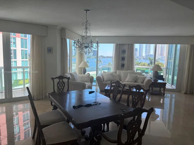 Expansive room featuring floor-to-ceiling windows, waterfront scenery, high-gloss tile flooring, and a crystal chandelier