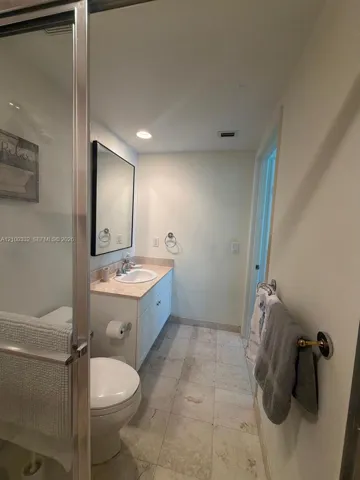 Walk-in shower with glass enclosure, single vanity with light-toned countertop, integrated sink, and tile flooring