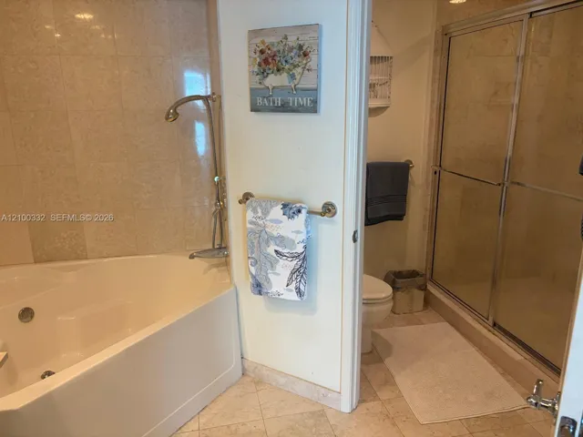 Corner soaking tub, tiled shower enclosure with sliding glass doors, and light-toned floor and wall tiling