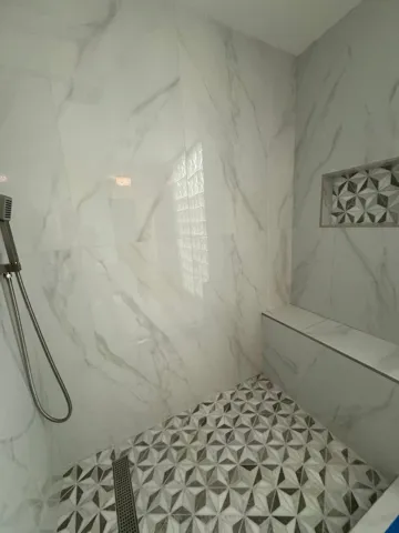 Tiled shower featuring porcelain walls, built-in bench, recessed shelf with mosaic tile, and a handheld shower fixture