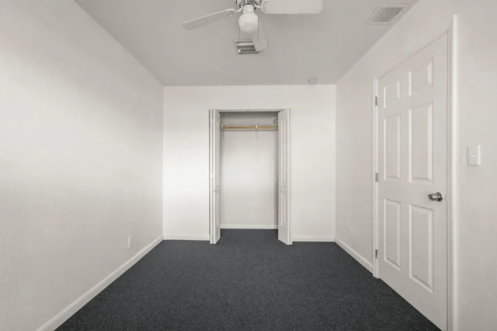 Neutral wall color, dark carpeting, and a ceiling fan